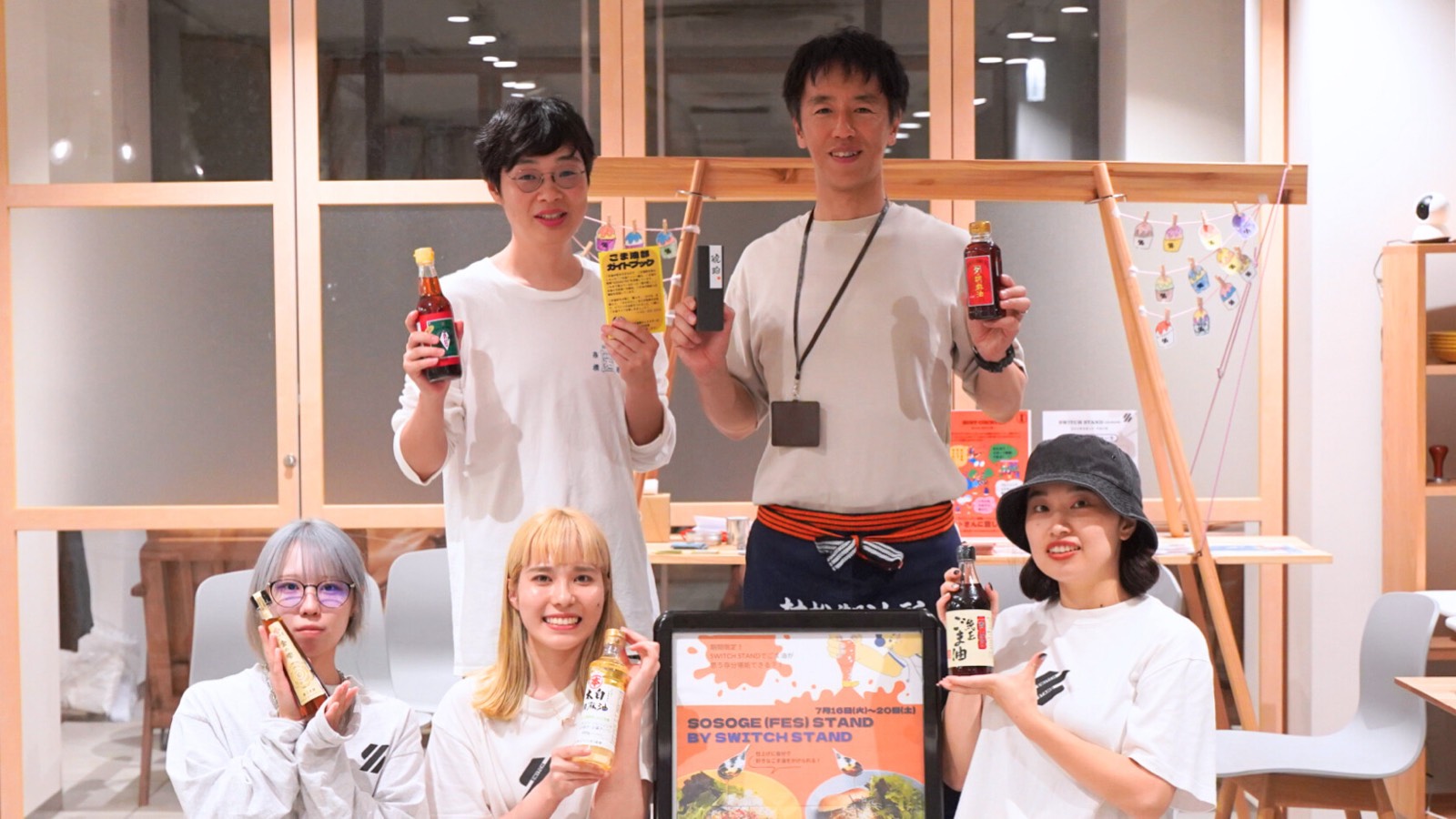 「SOSOGE FES」の出店の様子。5人のスタッフがそれぞれごま油の瓶やガイドブックを手に持って並んでいる