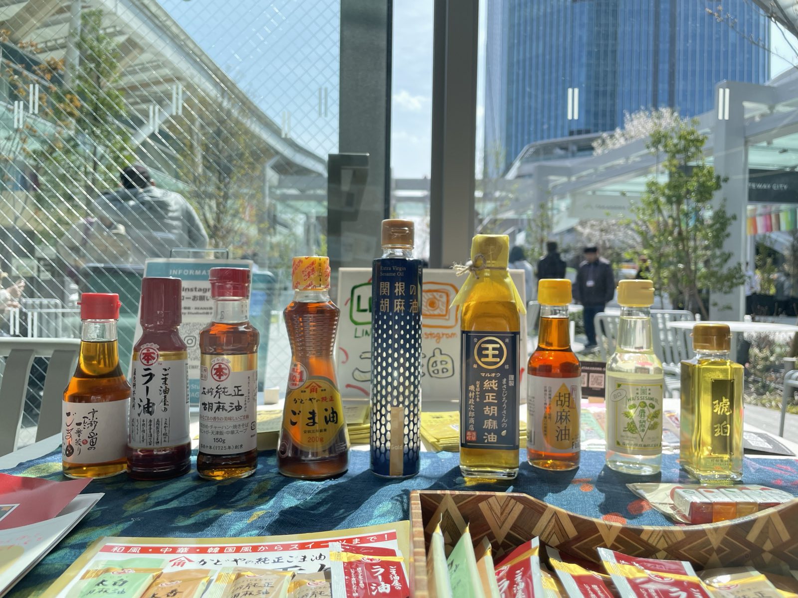 卓上に並んだ全国のごま油。瓶の形もラベルの色もさまざまで、手書きの「ごま油部」の看板が置かれている